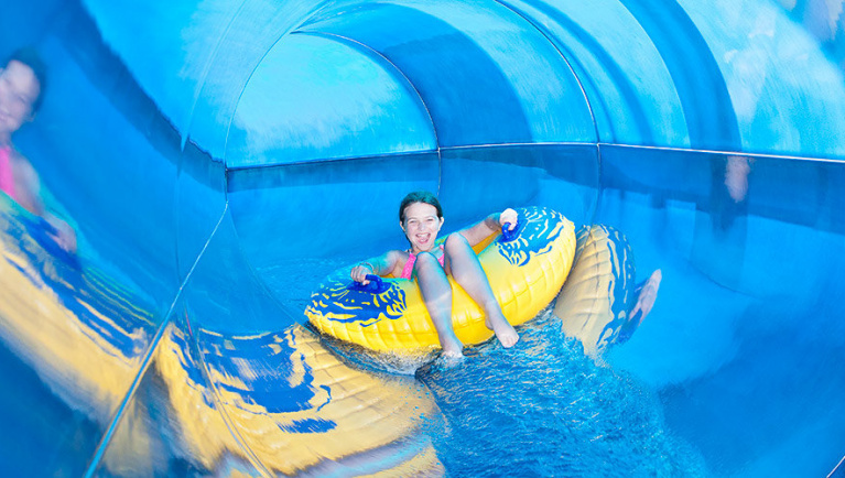 A girl smiles at the camera as she rides a tube down a water slide at a Great Wolf Lodge indoor water park.